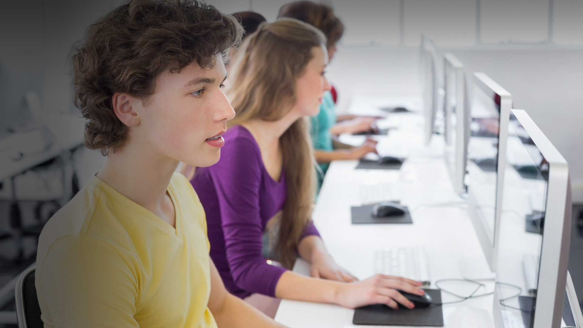 A imagem sugere a aplicação da prova do PISA 2025 em uma sala de aula com alguns estudantes com seus notebooks e uma professora.